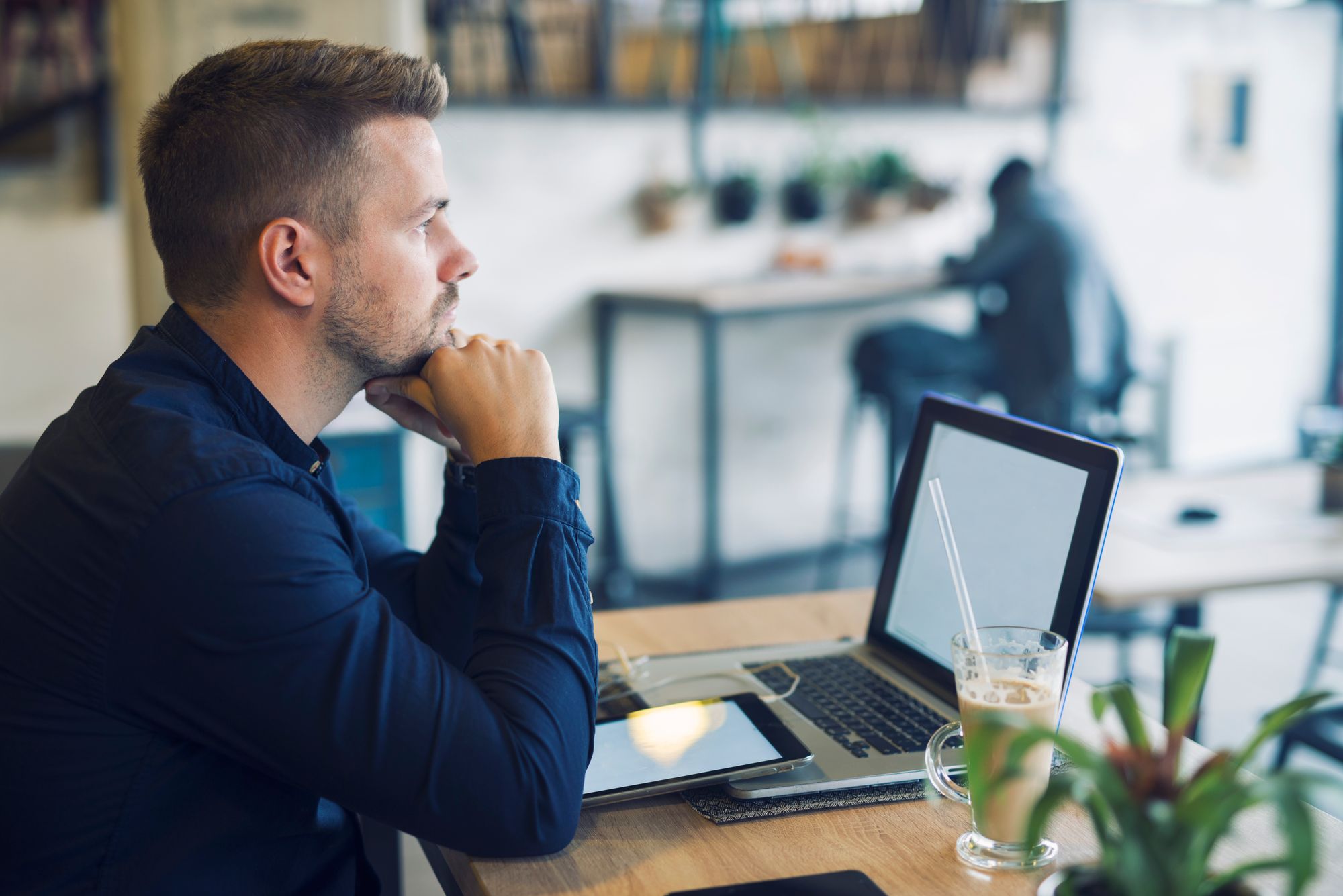 Homem sentado em frente a laptop e tablet, com um café ao lado, tem dúvidas sobre como funciona plano de saúde com coparticip